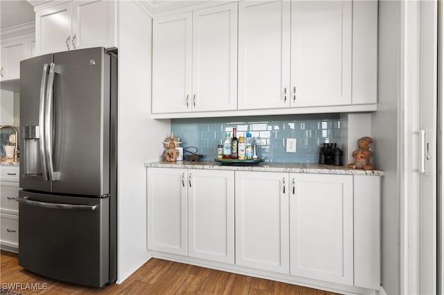 bar with tasteful backsplash, stainless steel fridge, light stone countertops, and white cabinets