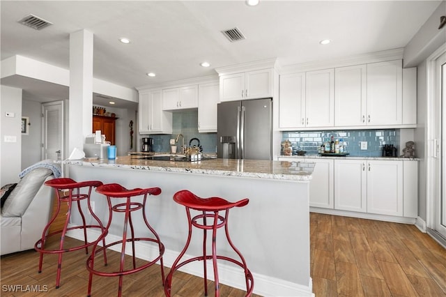 kitchen featuring white cabinetry, light stone countertops, stainless steel fridge with ice dispenser, kitchen peninsula, and light wood-type flooring