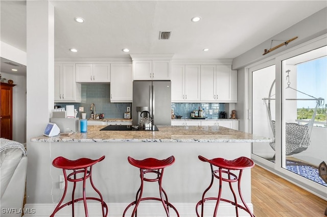 kitchen with white cabinetry, light wood-type flooring, light stone countertops, and stainless steel refrigerator with ice dispenser