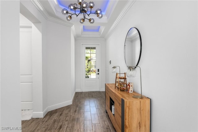 doorway to outside featuring a raised ceiling, crown molding, and an inviting chandelier