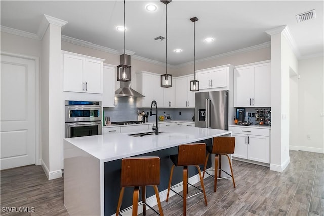 kitchen with white cabinetry, sink, wall chimney range hood, a center island with sink, and appliances with stainless steel finishes