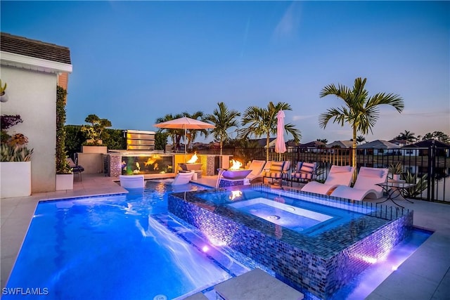 pool at dusk with an in ground hot tub, pool water feature, and a patio