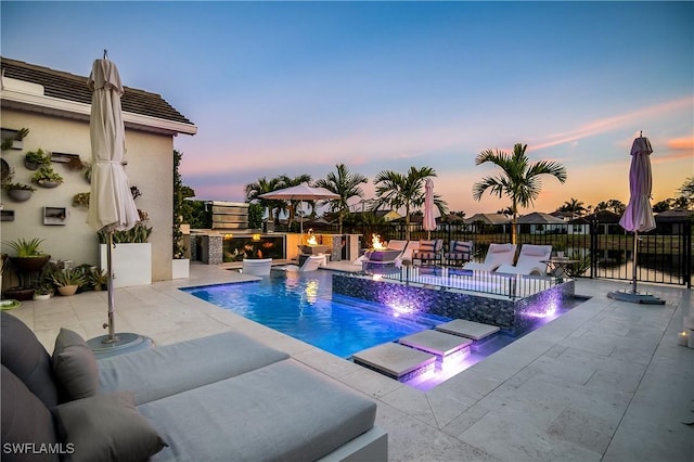 pool at dusk featuring pool water feature, a patio, and a hot tub