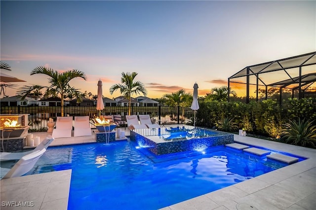 pool at dusk with an in ground hot tub, pool water feature, a patio, and an outdoor fire pit