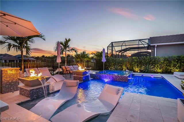 pool at dusk featuring pool water feature, a patio, an in ground hot tub, and an outdoor fire pit