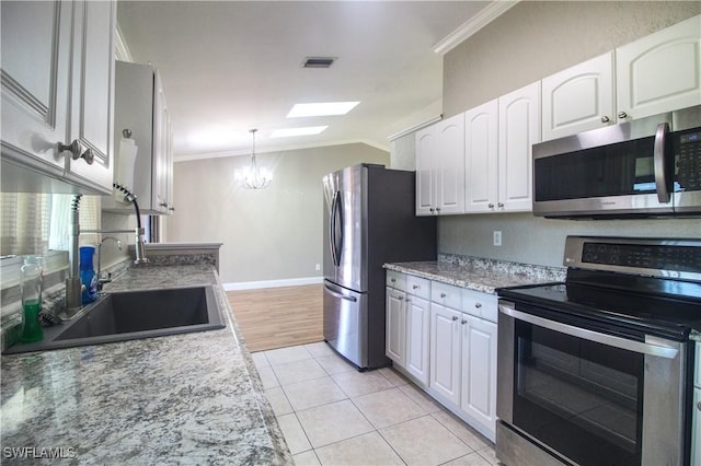 kitchen with a skylight, light tile patterned floors, appliances with stainless steel finishes, light stone counters, and white cabinetry