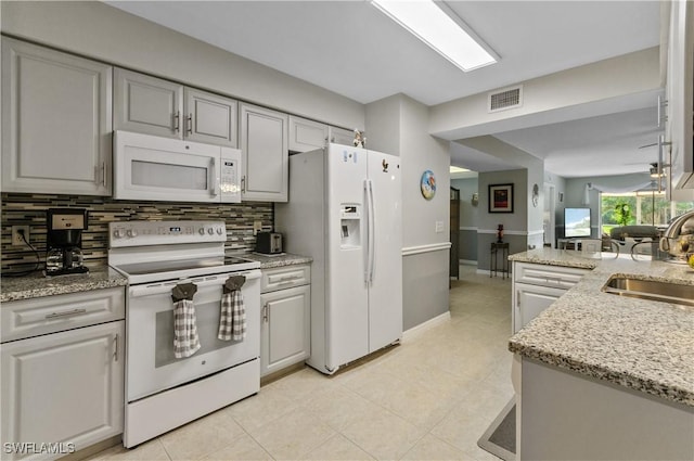 kitchen with light tile patterned floors, tasteful backsplash, white appliances, light stone countertops, and sink