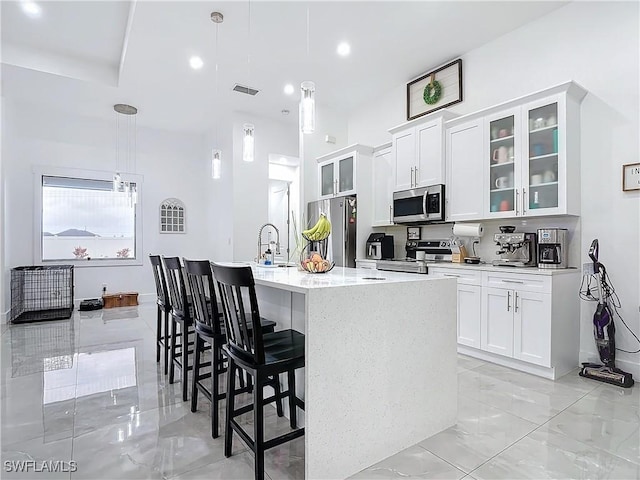 kitchen featuring white cabinets, hanging light fixtures, appliances with stainless steel finishes, and an island with sink