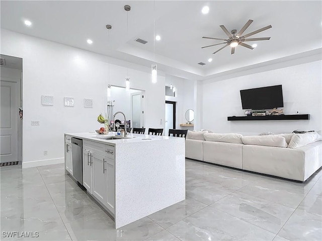 kitchen with a raised ceiling, a kitchen island with sink, sink, decorative light fixtures, and white cabinetry