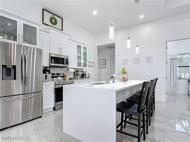 kitchen featuring appliances with stainless steel finishes, decorative light fixtures, a center island with sink, white cabinets, and a breakfast bar area