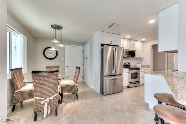 kitchen with light stone countertops, a healthy amount of sunlight, hanging light fixtures, stainless steel appliances, and white cabinets