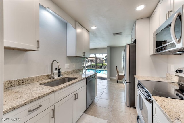 kitchen featuring white cabinets, sink, light tile patterned floors, appliances with stainless steel finishes, and light stone counters