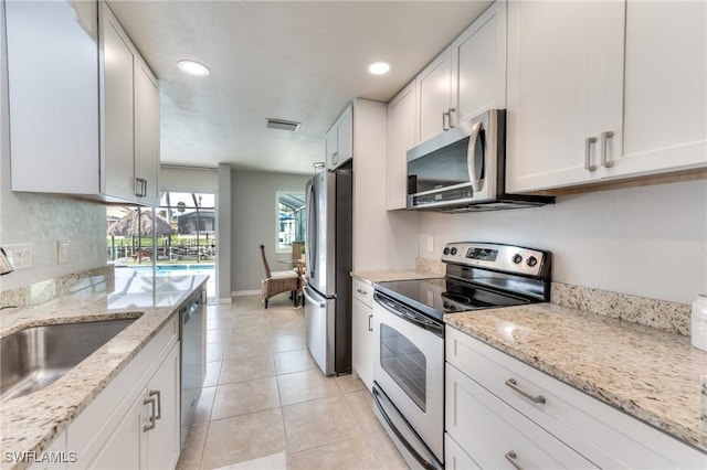 kitchen with sink, light stone counters, light tile patterned flooring, white cabinets, and appliances with stainless steel finishes