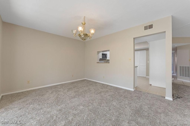 carpeted empty room with an inviting chandelier