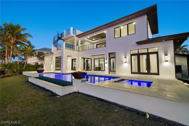 back house at dusk with a swimming pool with hot tub, a yard, a balcony, and a patio