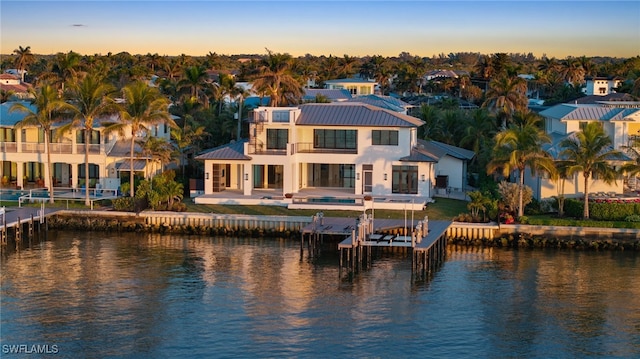 back house at dusk with a patio area, a balcony, and a water view