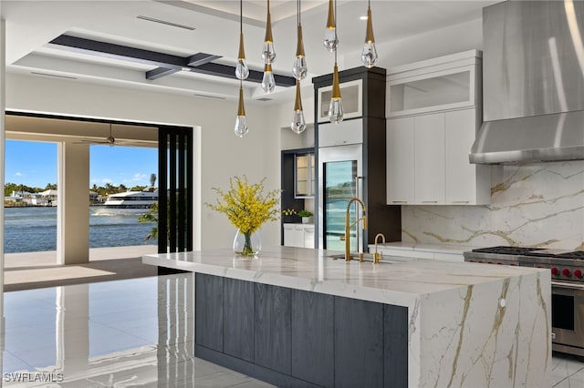 kitchen with white cabinetry, high end range, wall chimney exhaust hood, tasteful backsplash, and a large island with sink