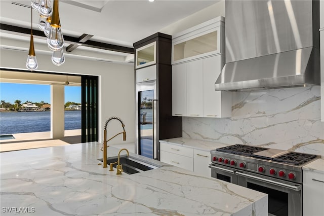 kitchen featuring range with two ovens, decorative light fixtures, backsplash, a sink, and wall chimney range hood