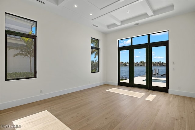 unfurnished room with beam ceiling, light wood finished floors, a water view, coffered ceiling, and baseboards