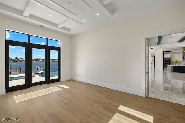 spare room featuring beamed ceiling, a water view, light wood-style flooring, and baseboards