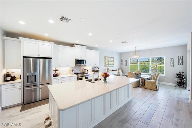 kitchen with a kitchen island with sink, stainless steel appliances, light countertops, and white cabinetry