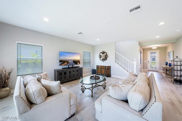 living area featuring light wood-style floors, visible vents, and stairway