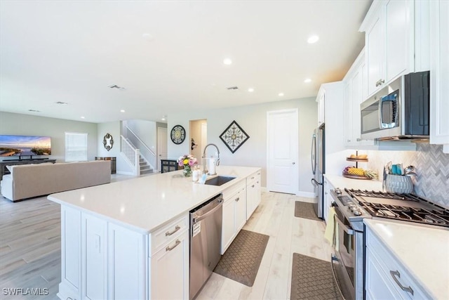 kitchen featuring a kitchen island with sink, stainless steel appliances, a sink, and light countertops