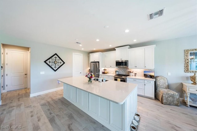 kitchen with an island with sink, white cabinets, and stainless steel appliances