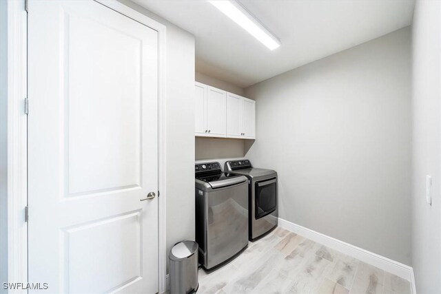 clothes washing area featuring cabinets, washing machine and dryer, and light hardwood / wood-style flooring