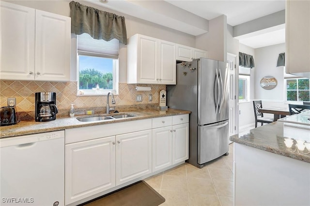 kitchen featuring white dishwasher, sink, tasteful backsplash, white cabinetry, and stainless steel refrigerator