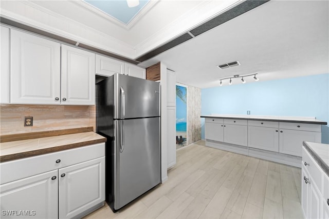 kitchen with wood counters, crown molding, stainless steel fridge, light wood-type flooring, and white cabinetry