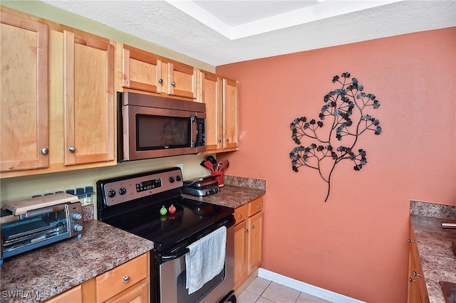 kitchen with a textured ceiling, dark stone countertops, light tile patterned floors, and appliances with stainless steel finishes