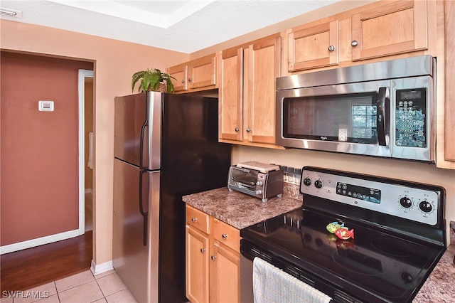 kitchen with stainless steel appliances, stone countertops, light brown cabinetry, and light tile patterned flooring