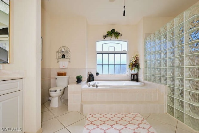 bathroom with tile patterned floors, toilet, tile walls, vanity, and tiled tub