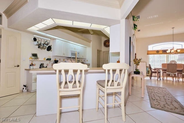 kitchen featuring white cabinetry, a breakfast bar area, a chandelier, light tile patterned floors, and kitchen peninsula