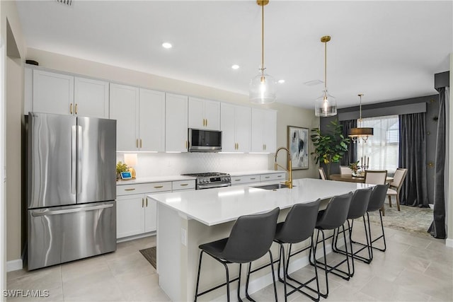 kitchen featuring sink, stainless steel appliances, a kitchen island with sink, and hanging light fixtures