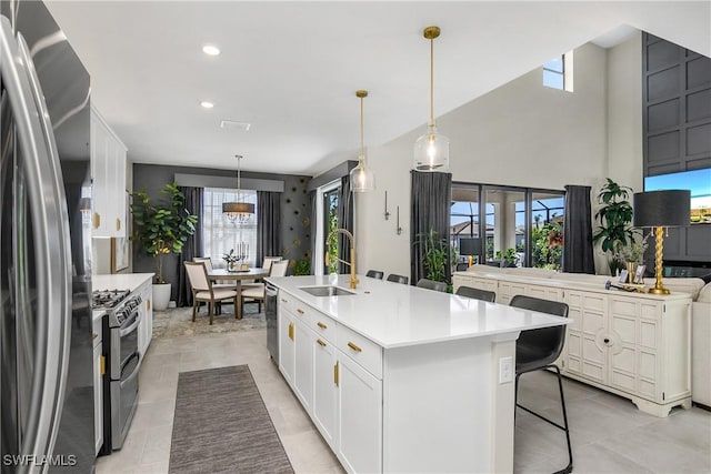 kitchen with white cabinets, a center island with sink, stainless steel appliances, sink, and decorative light fixtures