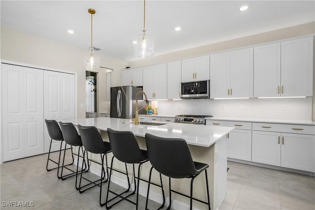 kitchen featuring appliances with stainless steel finishes, white cabinetry, a kitchen island with sink, and hanging light fixtures