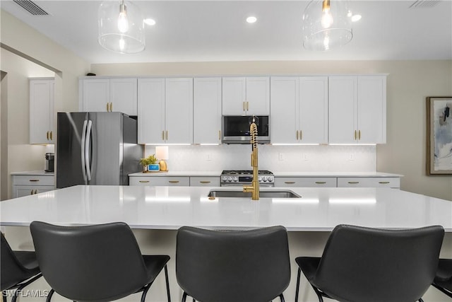 kitchen featuring stainless steel appliances, a kitchen island with sink, pendant lighting, and sink