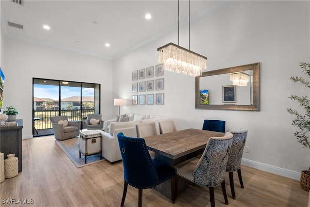 dining space with light hardwood / wood-style floors, a towering ceiling, crown molding, and an inviting chandelier