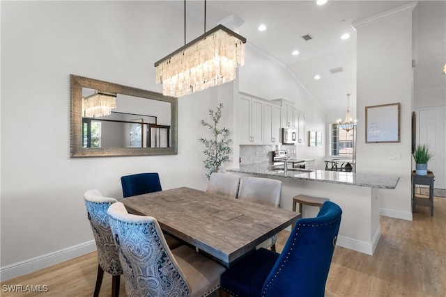 dining room with a notable chandelier, light hardwood / wood-style flooring, lofted ceiling, and ornamental molding