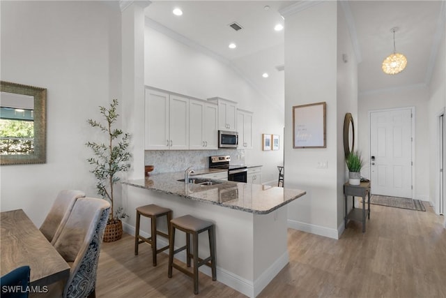 kitchen featuring light stone countertops, white cabinetry, stainless steel appliances, kitchen peninsula, and decorative light fixtures