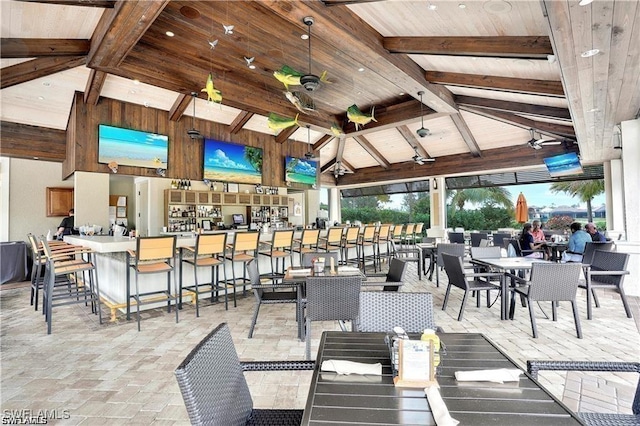 dining room featuring ceiling fan, high vaulted ceiling, wooden ceiling, beamed ceiling, and wood walls