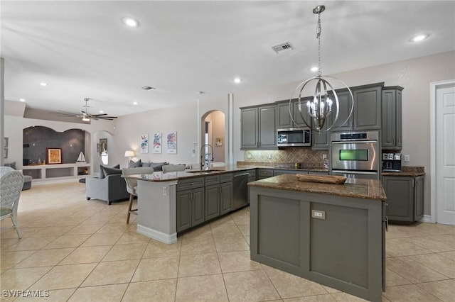 kitchen featuring an island with sink, gray cabinets, ceiling fan with notable chandelier, appliances with stainless steel finishes, and light tile patterned flooring