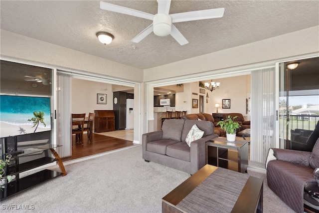 carpeted living room with ceiling fan with notable chandelier and a textured ceiling