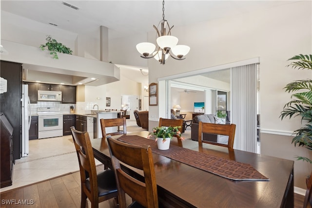 dining space featuring a high ceiling, ceiling fan with notable chandelier, light hardwood / wood-style flooring, and sink