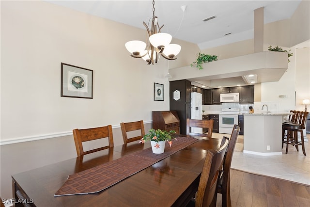 dining room with sink, light hardwood / wood-style flooring, a towering ceiling, and a notable chandelier