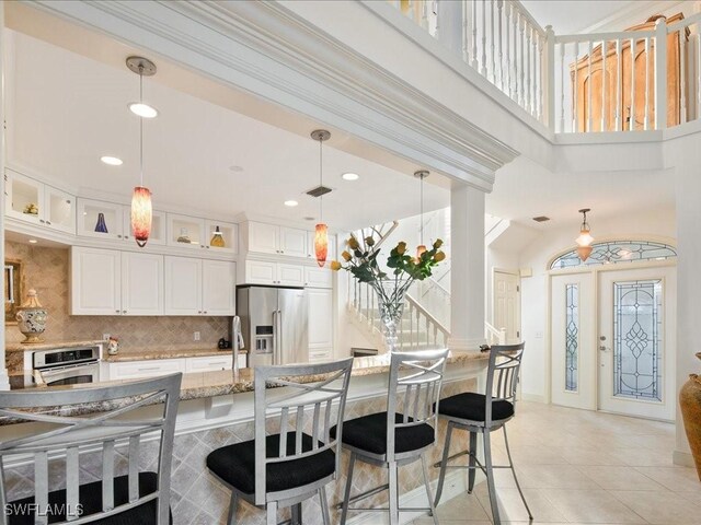 kitchen featuring white cabinets, light stone countertops, appliances with stainless steel finishes, tasteful backsplash, and decorative light fixtures