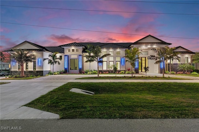 view of front of house featuring a front lawn, stucco siding, metal roof, driveway, and a standing seam roof