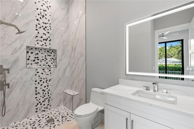 full bath with a tile shower, toilet, ceiling fan, and vanity